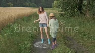 两个穿着靴子的快乐女孩姐妹在乡间小路上的雨水中嬉戏